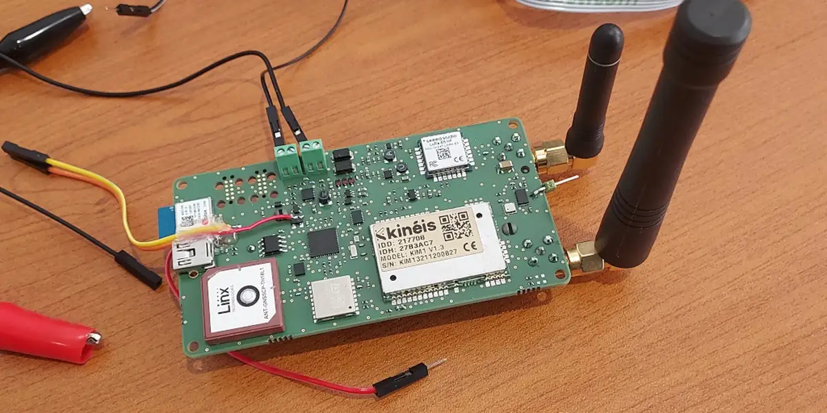 Carte de développement IoT Kinéis avec antennes BLE et SMA, branchée sur table de mesure.
