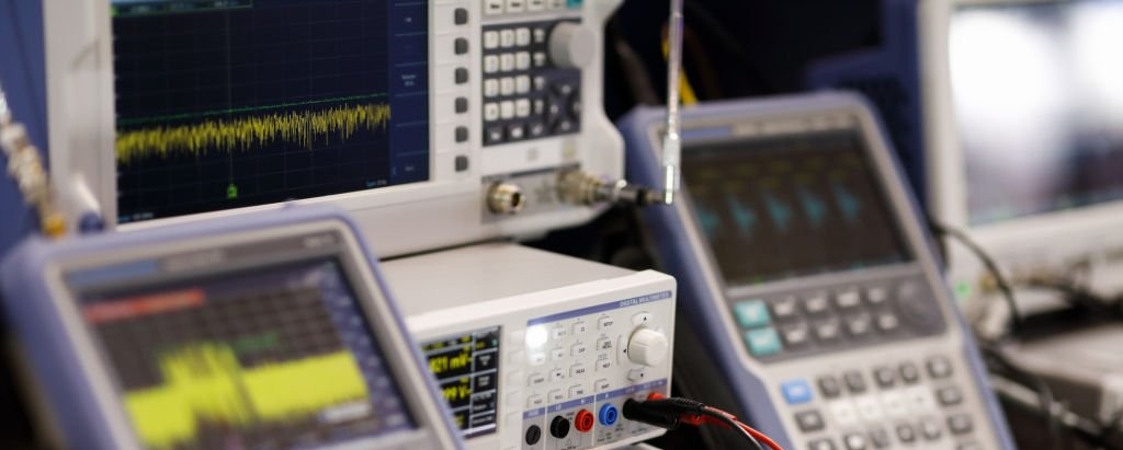 Typical electronic-design-house measurement bench: spectrum analyzer, digital oscilloscope and multimeter. Instrumentation used to characterise serial buses and audit signal integrity on embedded products.