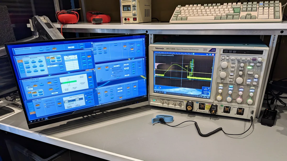 Banc de mesure intégrité de signal AESTECHNO Montpellier : oscilloscope Tektronix DPO 7104C avec moniteur Iiyama affichant TekExpress, alimentation Korad, et clavier mécanique sous bracelet antistatique.
