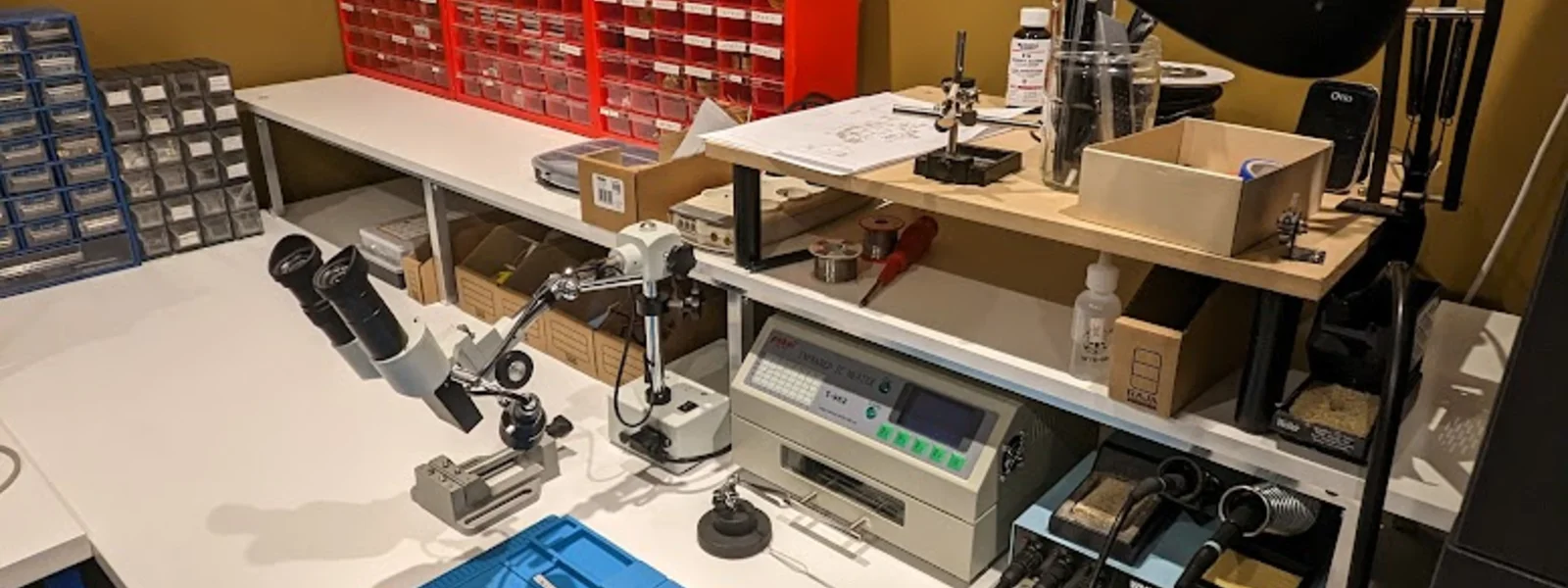 Atelier d'industrialisation AESTECHNO : four à refusion T962, station de soudage Weller, microscope d'inspection, et casiers de composants triés pour qualification IPC-A-610 et DFM.